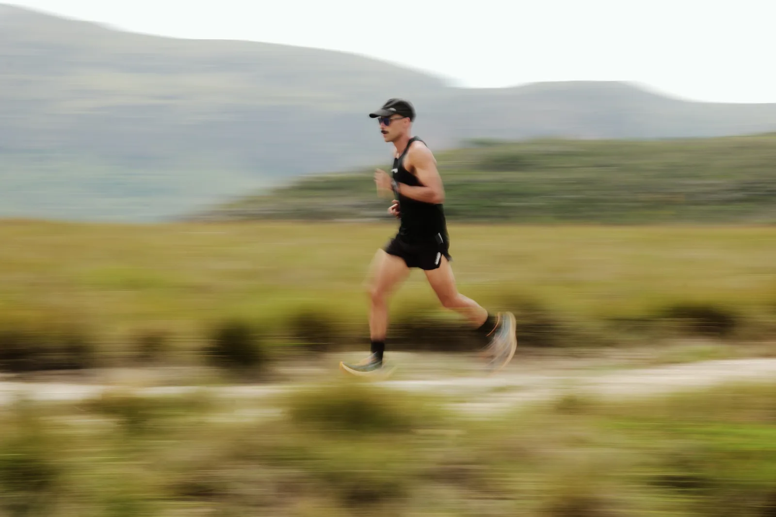 Corredor de Trail Run em movimento numa trilha de montanha, em meio a vegetação de campo